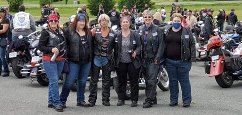 Group of women in biker gear posing for picture at bike rally with motorcycles in background